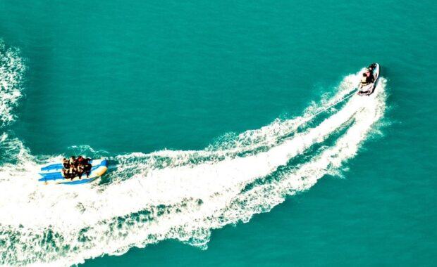 A banana boat with a group of people on it being pulled through the water by a Jet Ski